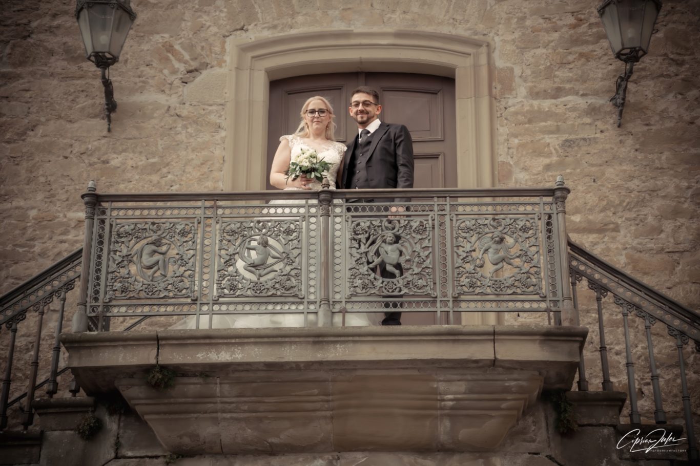 Hochzeitspaar steht lächelnd vor einer Tür auf einem Balkon.